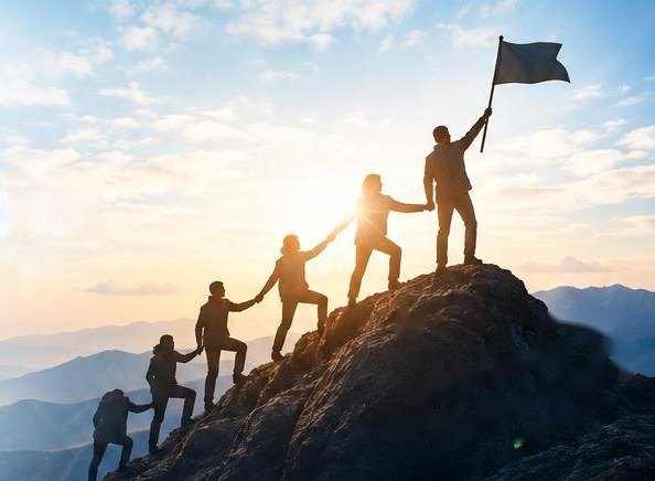 A team helping each other climb to a mountain summit at sunrise